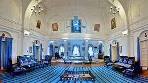 A spacious room with a central seating area, multiple windows, and a chandelier. - Neemrana's - Hill Fort - Kesroli (Ramgarh)