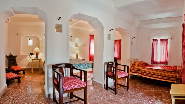 A room with a bed, two wooden chairs, a small table, and a lamp. - Neemrana's - Hill Fort - Kesroli (Ramgarh)
