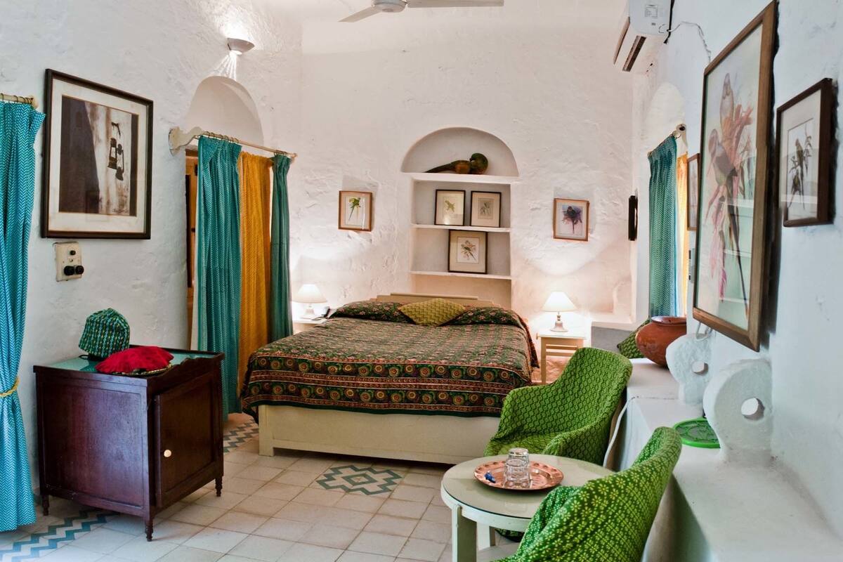 A bedroom with a bed, a chair, a table, a shelf with pictures, and a ceiling fan.