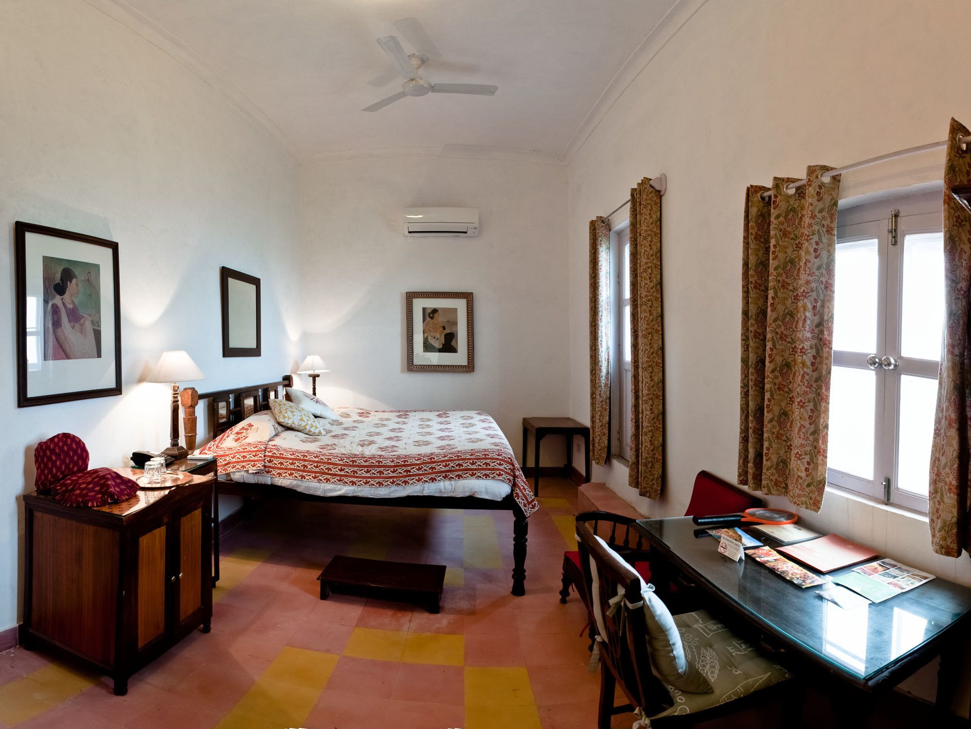 A bedroom with a bed, bedside table, lamp, chair, desk, and window with curtains.