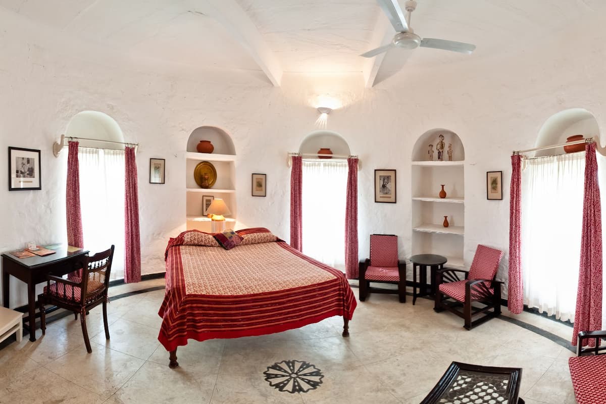 A room with a bed, a desk, chairs, shelves, and a ceiling fan.