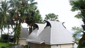 Una casa con un diseño de techo inclinado único, rodeada de exuberante follaje y palmeras.