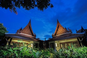 A symmetrical building with pointed roofs and intricate carvings, surrounded by lush greenery. - Anavana Beach Resort (Koh Samui)