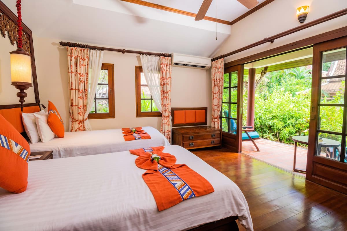 Habitación de hotel con dos camas, un aparador de madera y un amplio ventanal corredero que da a un espacio exterior.