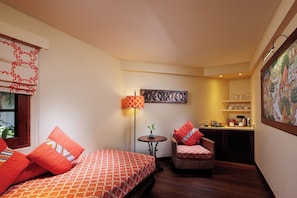 A compact room with two beds, a small table, a chair, a lamp, and a wall-mounted shelf with items. - Anavana Beach Resort (Koh Samui)