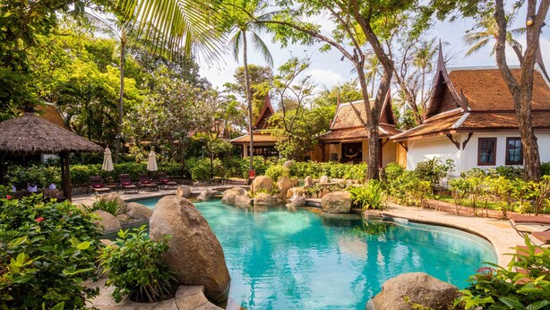 A pool surrounded by rocks and lush greenery, with traditional architecture in the background. - Anavana Beach Resort (Koh Samui)