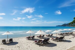 Uma praia com fileiras de espreguiçadeiras e guarda-sóis, céu claro e mar calmo.