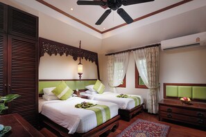 A hotel room with two beds, a ceiling fan, a window with curtains, a bedside table, and a dresser. - Anavana Beach Resort (Koh Samui)
