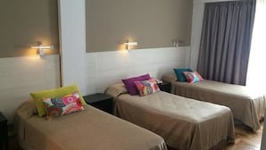 Habitación de hotel con dos camas individuales, cada una con un cojín de colores y una mesita de noche.
