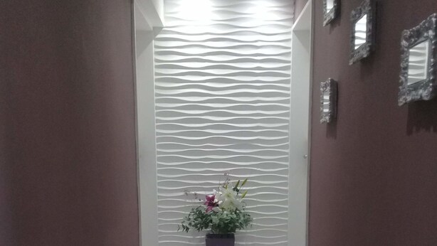 Un pasillo con piso de madera, un panel decorativo en la pared y una planta en maceta con flores.