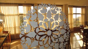 Una habitación con un amplio panel decorativo en el centro, un comedor con sillas y una mesa, y ventanas grandes con cortinas.
