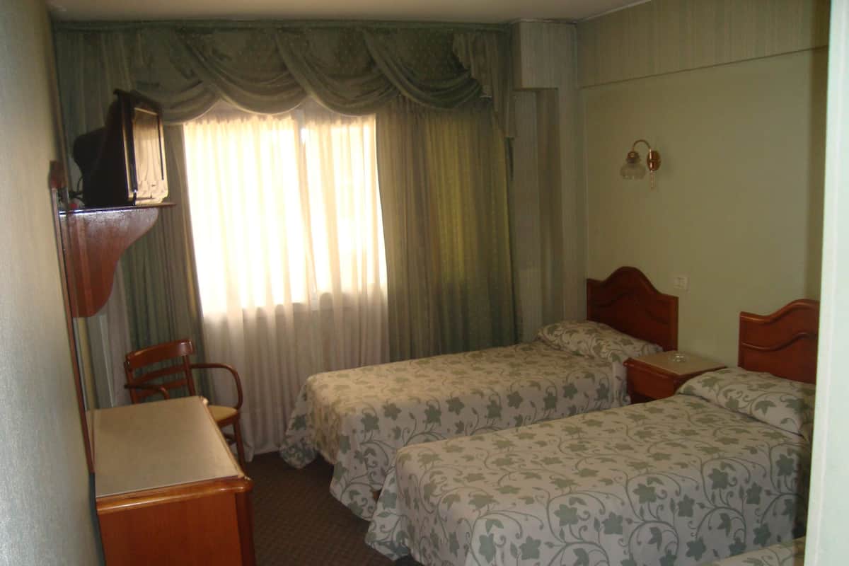 Habitación de hotel con dos camas, un escritorio de madera, una silla y una ventana con cortinas.