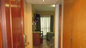 Un pasillo que conduce a un dormitorio con una cama, una silla y una mesita.