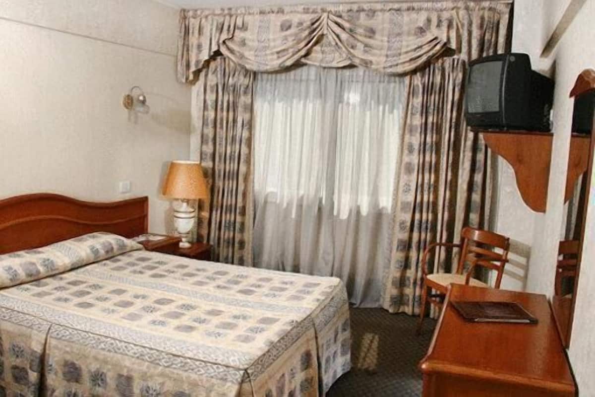 Una habitación de hotel con una cama, un escritorio, una silla, una lámpara y un televisor.