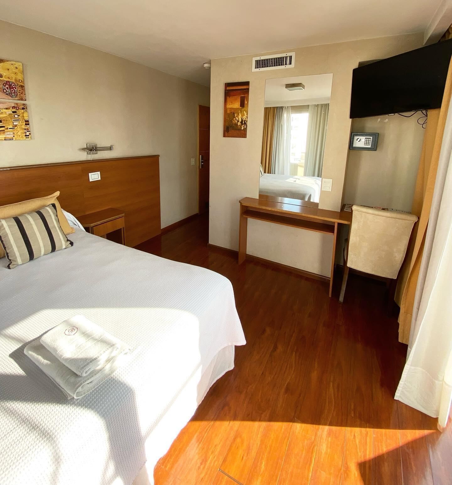 Una habitació d'hotel amb un llit, una taula de treball, un mirall i una finestra.