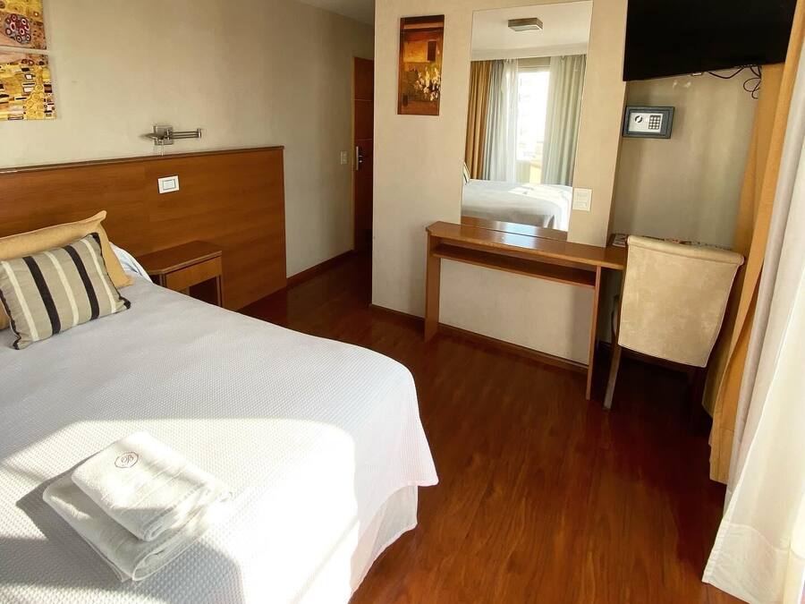 Una habitació d'hotel amb un llit, una taula de treball, un mirall i una finestra.