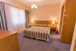A hotel room with a bed, two bedside tables, a wooden desk, a chandelier, and a door.