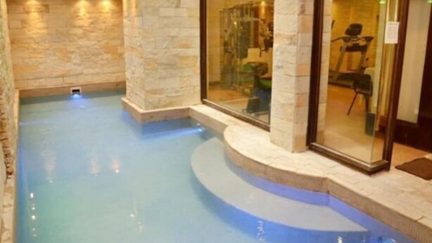 An indoor swimming pool with stone walls and glass doors leading to a fitness area. - Astor Hotel (MAR DEL PLATA)