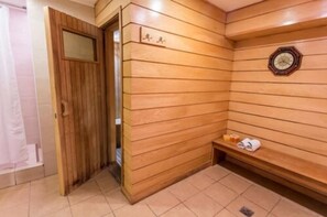 A wooden sauna room with a bench, a clock, and a small shelf with towels.