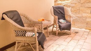 Two wicker chairs with black cushions, a small round table with a candle, and a stone wall in the background. - Astor Hotel (MAR DEL PLATA)