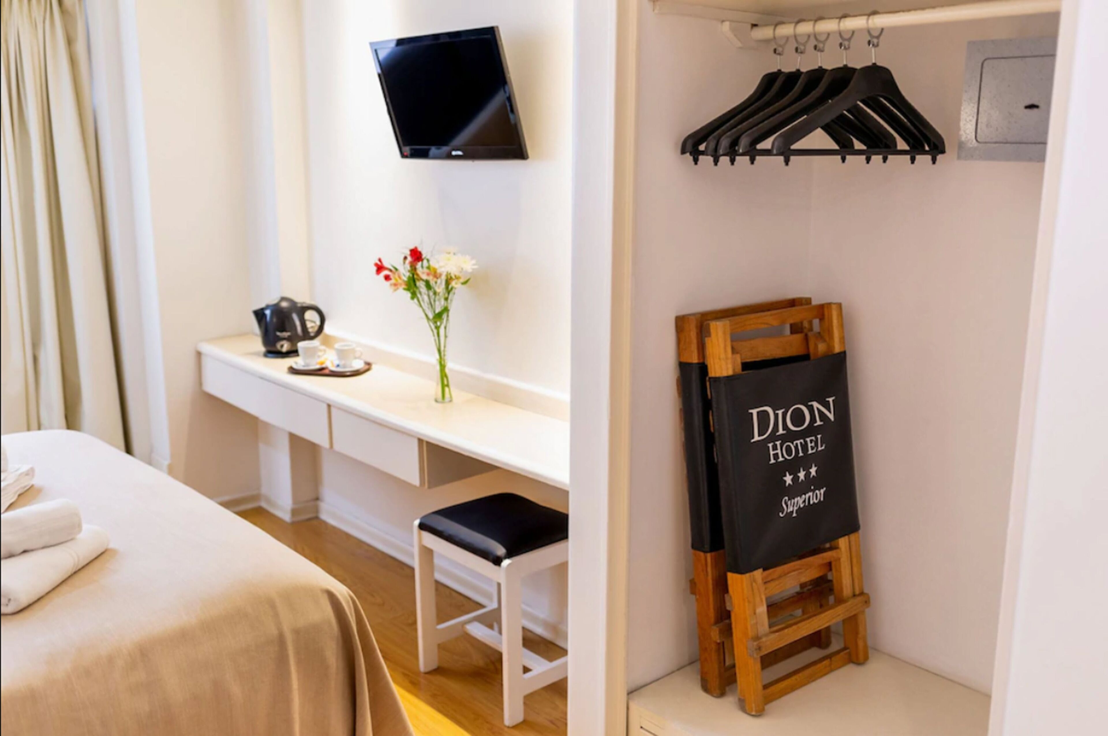 Habitación de hotel con cama, escritorio con cafetera, televisión y perchero con un cartel.