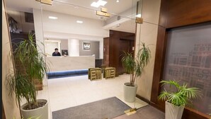 A hotel reception area with a reception desk, potted plants, and a large mirror. - Estocolmo Hotel (Mar del Plata)