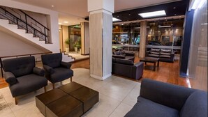 A modern living room with dark sofas, a coffee table, and a staircase. - Estocolmo Hotel (Mar del Plata)