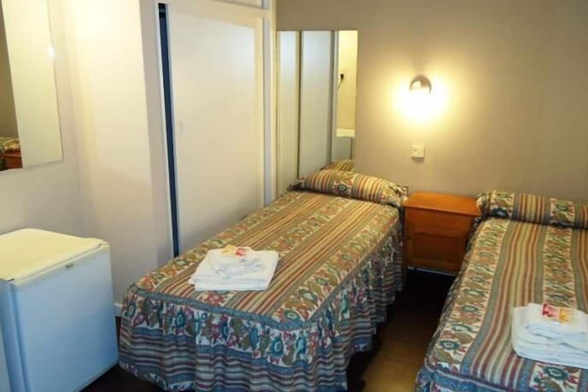 Une petite pièce, de taille modeste, comprenant deux lits simples, une petite table et un radiateur blanc.