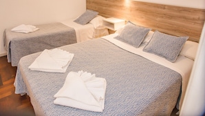 Une chambre d’hôtel avec deux lits, chacun doté d’une tête de lit en bois, de draps blancs et d’une petite table de chevet avec une lampe.
