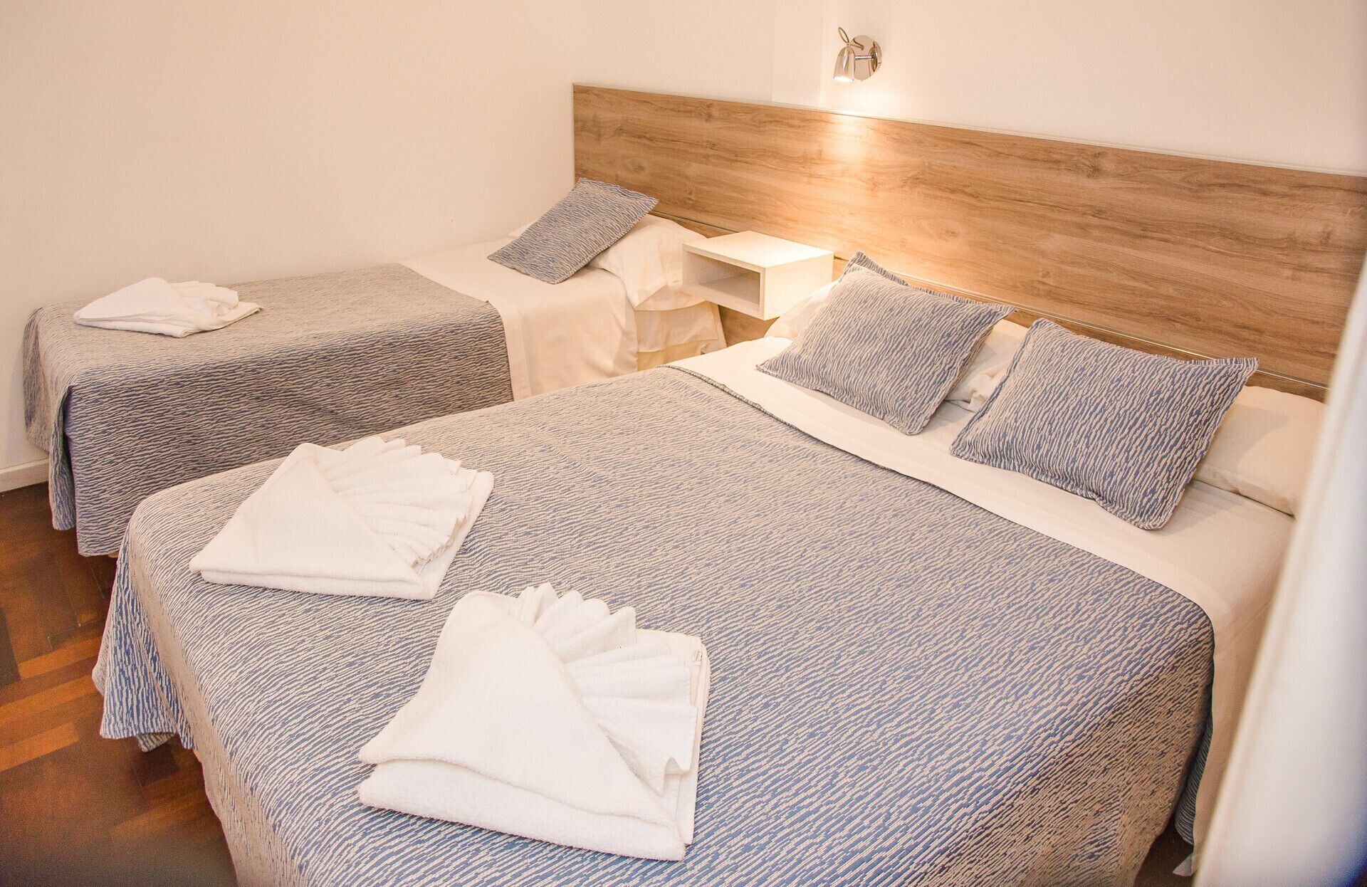Habitació d'hotel amb dos llits, cada un amb capçalera, una taula de nit i una làmpada penjada a la paret.