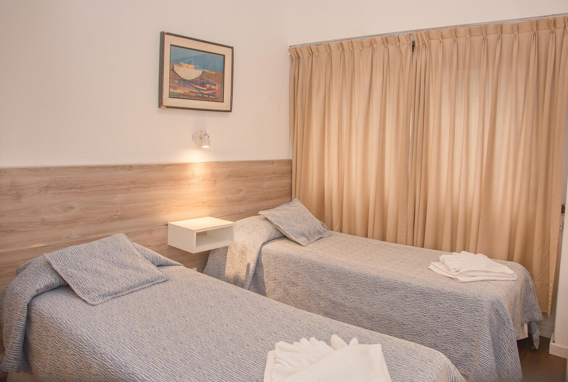 Habitación de hotel con dos camas, una mesita de noche, una lámpara de pared y un cuadro.