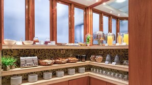 Un bufé de desayuno con diversas opciones de comida, una máquina de café y un dispensador de zumo.