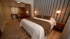 Habitación de hotel con una cama grande, un escritorio con silla, una pequeña kitchenette y un baño.