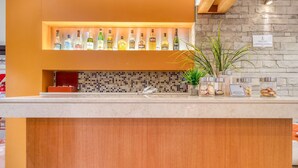 Una zona de bar con diversas botellas de licor, una planta en maceta y botes de frutos secos y fruta deshidratada sobre la barra.