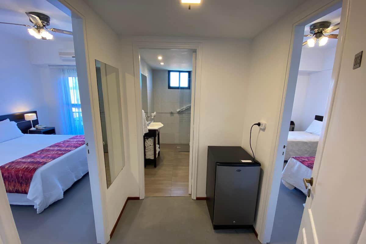 Ein Hotelzimmer mit zwei Betten, einem Schreibtisch, einem kleinen Kühlschrank und einem durch eine offene Tür einsehbaren Badezimmer.