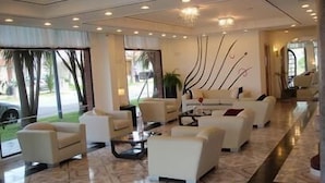 A modern hotel lobby with a marble floor, white sofas, and a large window offering a view of palm trees. - Montecarlo Hotel (Mar del Plata)