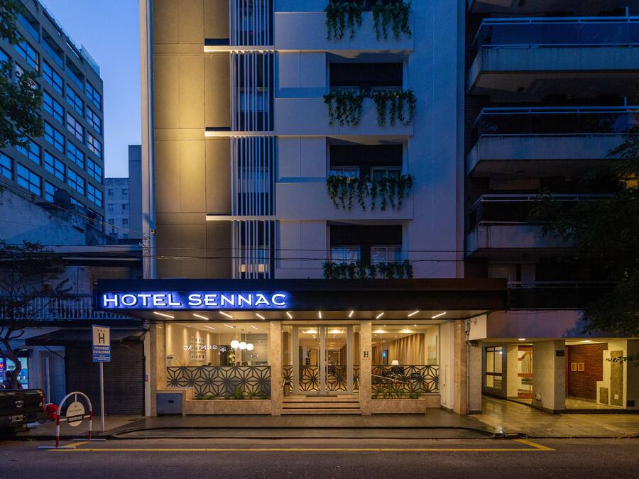 A hotel entrance with a sign reading "HOTEL SENNAC," a modern facade, and a gated entrance.