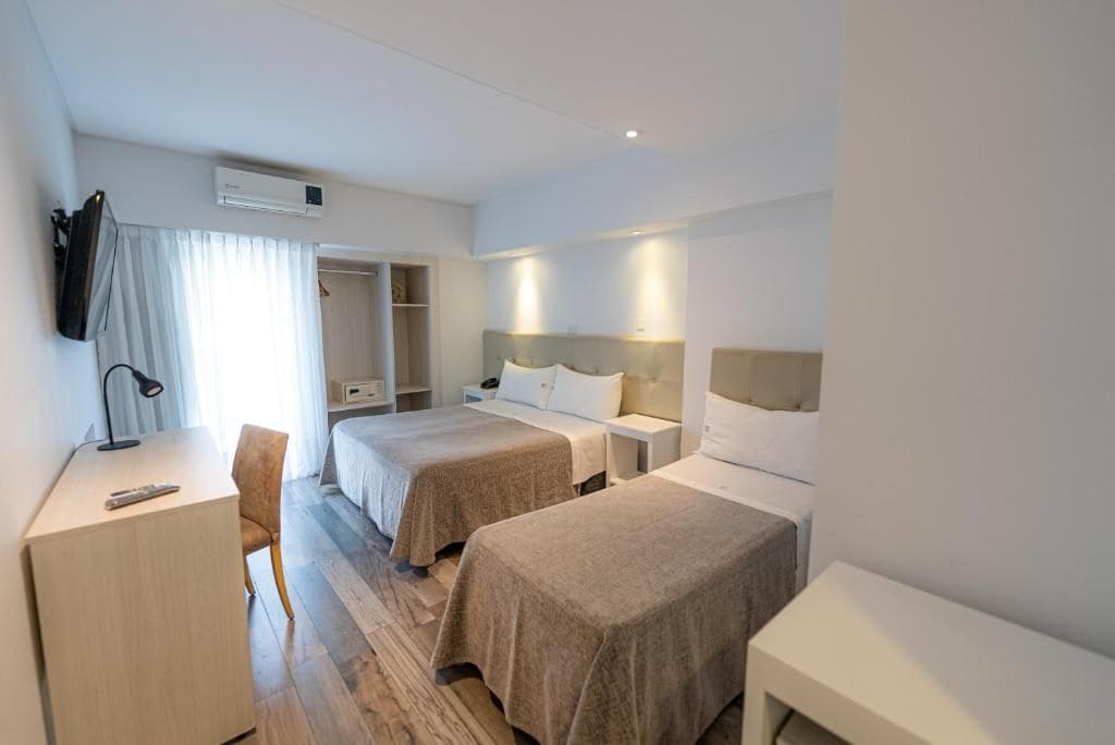 A hotel room with two beds, a desk, a chair, a wardrobe, and an air conditioning unit.
