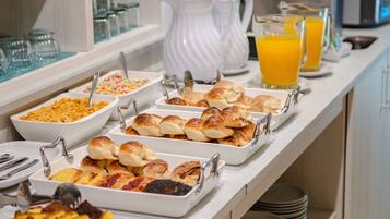 Buffet com diversos alimentos e um jarro de suco de laranja.