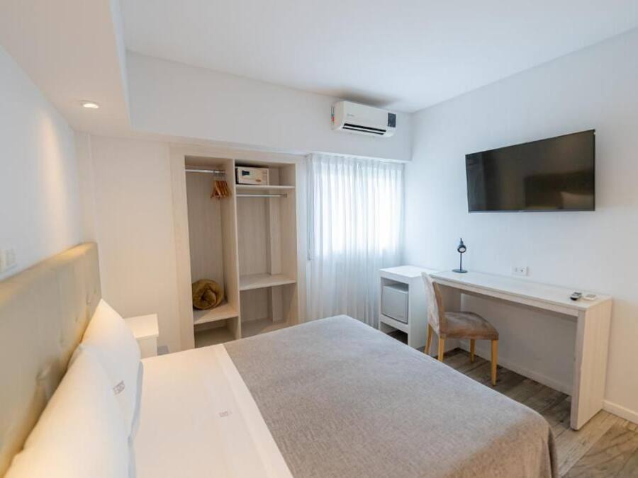 Una habitación de hotel con una cama, un escritorio, una silla, un televisor montado en la pared y un armario.