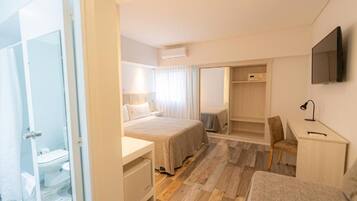 A hotel room with a bed, a desk, a chair, a TV, and a wardrobe.