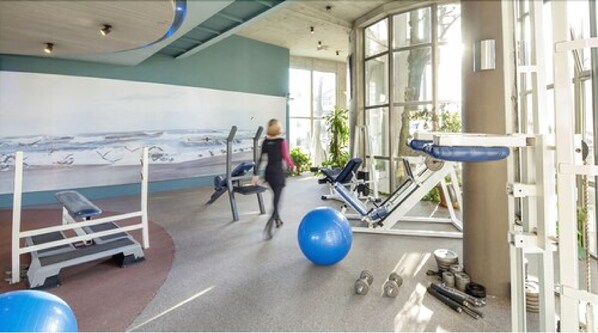 A gym with exercise equipment, a large blue exercise ball, and a mural of a beach scene.