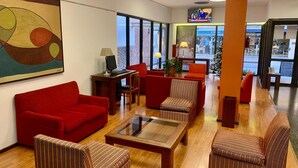 A modern lobby with red sofas, striped armchairs, a glass coffee table, and a large abstract painting on the wall. - Arenales Hotel (San Fernando del Valle de Catamarca)