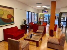 Un lobby moderno con sofás rojos, sillones a rayas, una mesa de centro de vidrio y un gran cuadro abstracto en la pared.