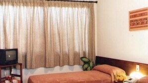 A hotel room with two beds, a television on a small table, and a window with curtains. - Arenales Hotel (San Fernando del Valle de Catamarca)
