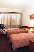 Una habitación de hotel con dos camas, un televisor sobre una mesita y una ventana con cortinas.