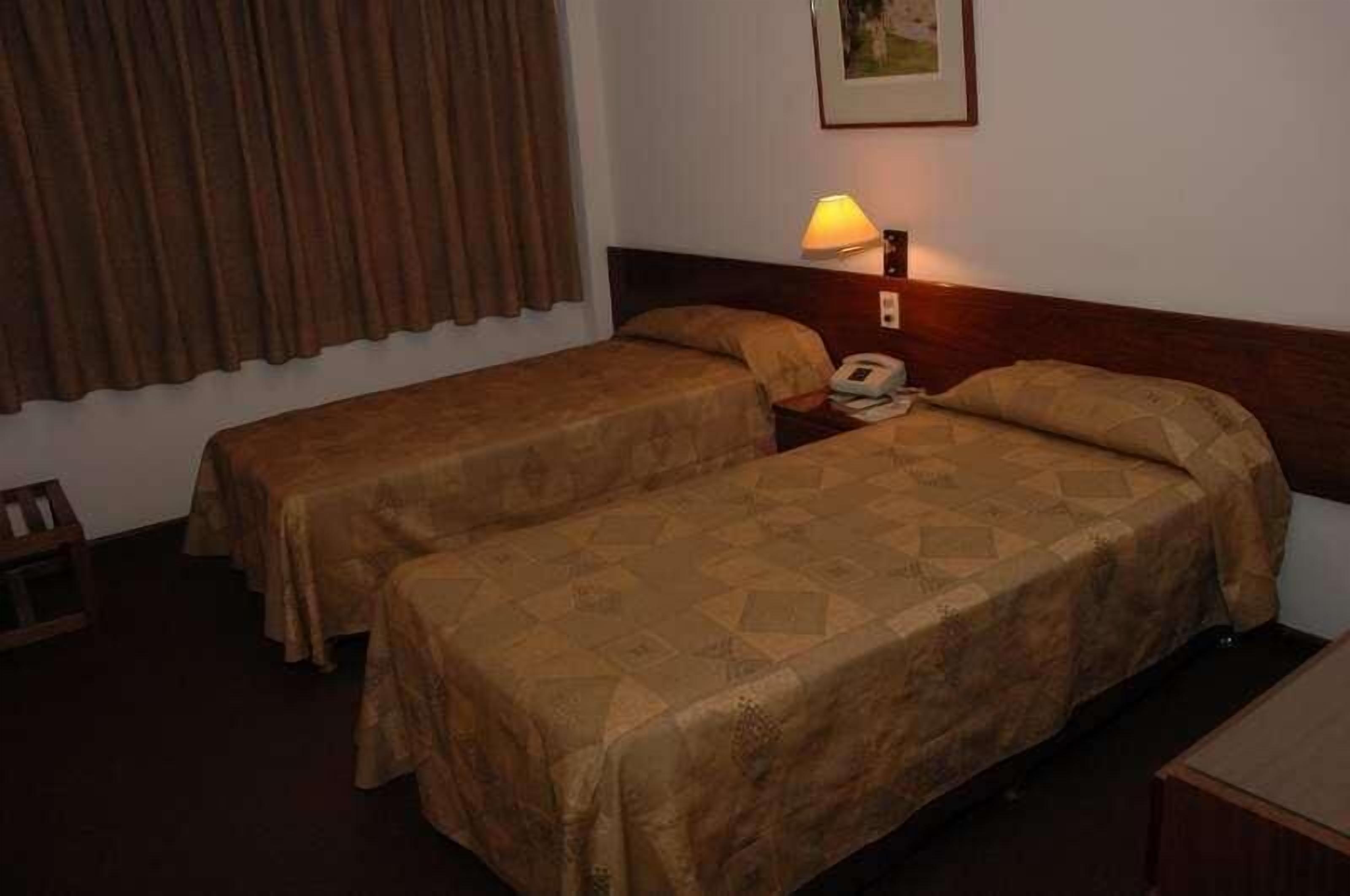 A hotel room with two single beds, a nightstand with a lamp, and a small table.