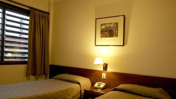 A hotel room with two beds, a bedside table with a lamp, a telephone, and a framed picture on the wall. - Arenales Hotel (San Fernando del Valle de Catamarca)