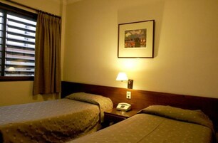 Habitación de hotel con dos camas, una mesita de noche con lámpara, teléfono y un cuadro enmarcado en la pared.