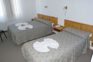 Habitación de hotel con dos camas individuales, cabecero de madera, mesita de noche con teléfono y radiador en la pared.